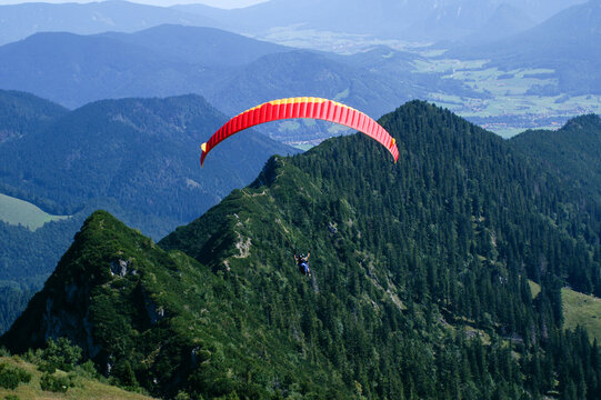 Paraglider tandem shortly after takeoff against wooded mountain ridge
