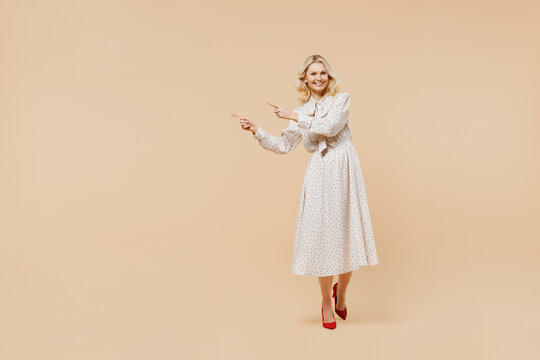 Full Size Body Length Elderly Gray-haired Blonde Woman Lady 40s Years Old Wears Pink Dress Point Aside On Workspace Area Copy Space Mock Up Isolated On Plain Pastel Beige Background Studio Portrait.