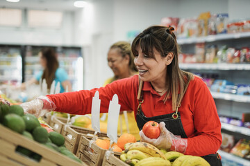 Mature latin woman working in a supermarket arranging fruits