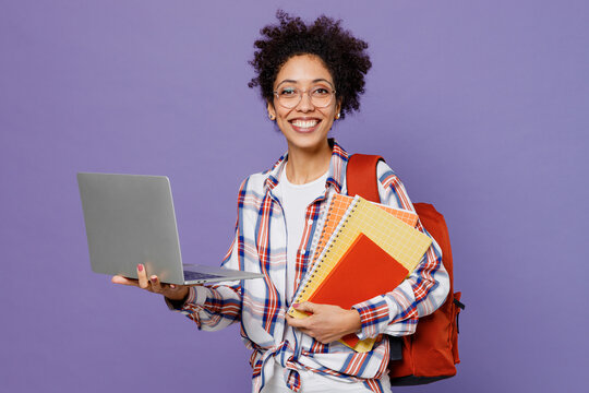 Young Girl Woman Of African American Ethnicity Teen Student 20s In Shirt Backpack Use Work On Laptop Pc Computer Isolated On Plain Purple Background Education In High School University College Concept