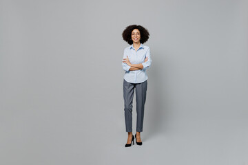 Full body smiling young employee business corporate lawyer woman of African American ethnicity in classic formal shirt work in office look camera hold hands crossed folded isolated on grey background.