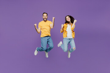 Full body overjoyed excited young couple two friends family man woman together wearn yellow casual clothes jump high do winner gesture clench fist isolated on plain violet background studio portrait.