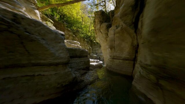 FPV drone extreme flying natural mountain river water splash surrounded by narrow textured cliff stones canyon landscape fast aerial view. Cold transparent clean waterfall wilderness nature scenery
