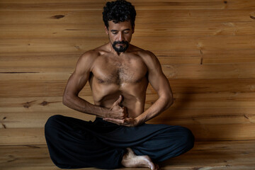 Latin American male yogi sitting practicing Nauli Kriya with Limgan Mudra. Concept of yoga and...