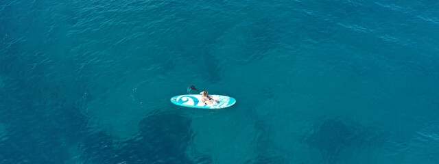 Aerial drone ultra wide panoramic photo with copy space of fit unidentified woman paddling on a SUP board or Stand Up Paddle board in deep blue sea