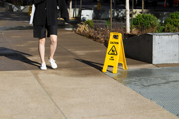 A person walking in a street nearby the yellow Caution Wet Floor Sign. Cleaning work