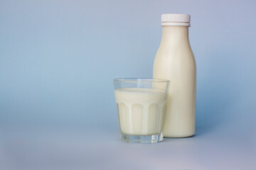 A glass and a bottle of white milk, highlighted on a blue background, close-up.