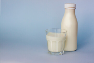 A glass and a bottle of white milk, highlighted on a blue background, close-up.
