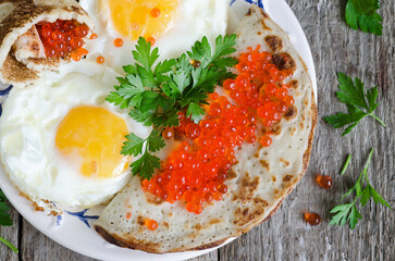 Fried eggs with pancakes and red caviar, close-up, on an old wooden background. View from above