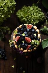 Savoyardi berry cake garnished with blackberries,blueberries and fresh figs on a wooden stand with hydrangea flowers on wooden table.Close up of cake in rustic style.
