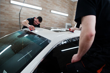 Worker in detailing garage put polyurethane anti-gravel film cover in white luxury car.