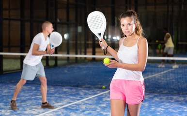 Young beautiful woman posing indoor on padel court with racket and ball