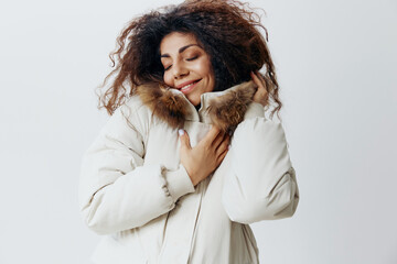 Smiling Enjoyed Curly Pretty Latin Woman Touching Soft Pastel Beige Warm Coat With Fur Hood Posing Isolated Closing Eyes At White Studio Wall Background. Fashion Huge Sale New Collection Concept