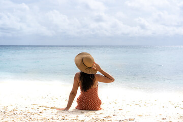 Young girl from the back in a straw hat on the background of the sea bay