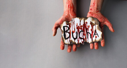 Bloody male hands hold a bloody and burnt paper with the inscription of the city of Bucha. The...