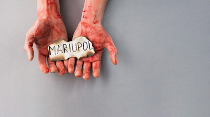 men's hands in blood hold a burnt paper with the inscription of the city of Mariupol. Killing of...