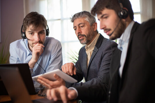 manager ou homme d'affaire d'&acirc;ge m&ucirc;r qui travaille au bureau avec deux jeunes employ&eacute;s ou stagiaires. Il donne des conseils. Il est chef d'&eacute;quipe. Ils travaillent avec des ordinateurs et une tablette