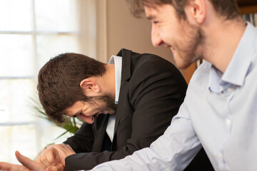 deux jeunes collègues, employés de bureau ou hommes d'affaires se détendent et rient tous les deux en travaillant au bureau. Ils sont complices