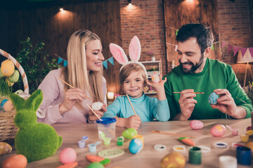 Photo of cheerful lovely family spend time indoors together mom and dad help son paint eggs prepare easter holiday