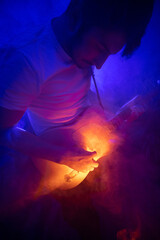 jeune homme qui joue de la guitare électrique en concert, dans une ambiance rock avec des lumières et de la fumée. Il prend du plaisir à jouer du rock et du blues.