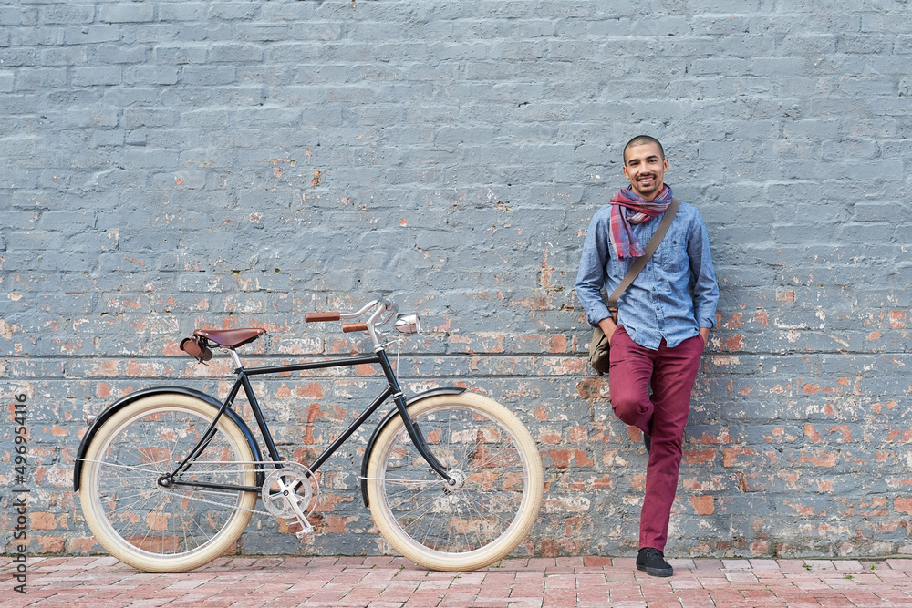 Poster why drive when you can cycle. portrait of a young man posing with his bicycle against a grey wall in