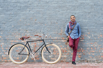 Why drive when you can cycle. Portrait of a young man posing with his bicycle against a grey wall...