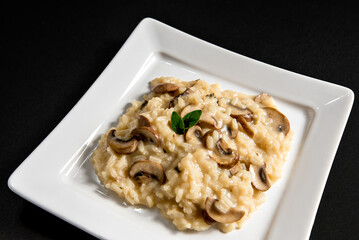 Risotto with mushroom on white plate on black background.