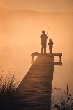 Beautiful morning scene by the lake. Father and son fishing in the light of the rising sun.