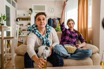 two people couple man and woman boyfriend and girlfriend or husband and wife sitting on the sofa at home watching football soccer game cheering copy space nervous anticipation and suspense