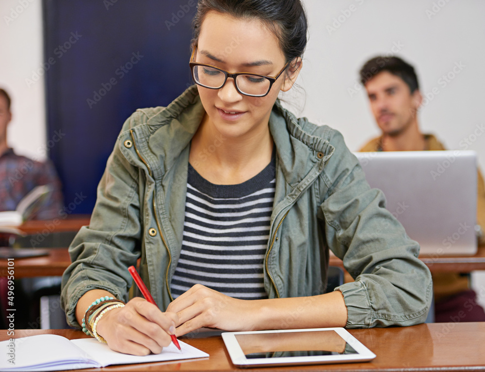 Poster doing the work to achieve her dreams. cropped shot of a young woman using notes and digital tablet i