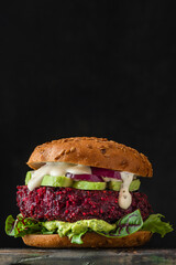 Vegan beetroot burger with avocado, onion, mayonnaise and salad on black background. vertical...