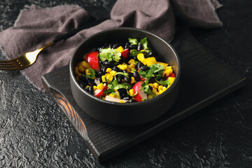 Wooden board with bowl of Mexican vegetable salad on dark background