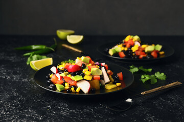 Plate of Mexican vegetable salad with black beans and radish on dark background