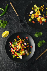 Plates of tasty Mexican vegetable salad with black beans and radish on dark background