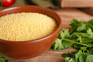 Bowl of raw couscous with parsley on table, closeup
