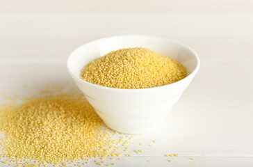 Bowl of raw couscous on white wooden background
