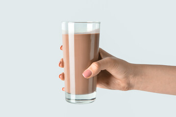 Female hand holding glass of delicious chocolate milk on grey background - Powered by Adobe