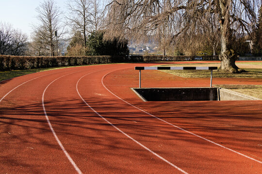 sportanlage munot schaffhausen switzerland: big red round track with water hurdle, weeping willow in the right edge of the picture, sport is healthy for young and old, without people, autumn day