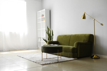 Interior of light living room with green sofa, pouf and lamp