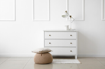 Beige pouf with pillow and chest of drawers near white wall