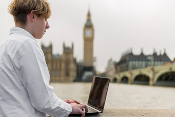 Close up portrait of student with laptop in London  stands on the riverside, London parliament on...