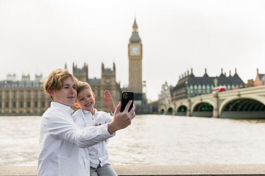 students with phone in London  stands on the riverside, London parliament on the background , brothers taking selfie at Big Ben, London