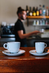 Detail shot of two white coffee cups on the bar counter. Waiting to be served to the customers.