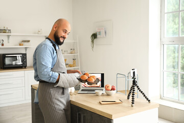 Handsome man with tasty peach muffins recording video tutorial in kitchen