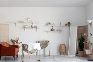 Interior of stylish room with armchairs, mirror and decor on shelves