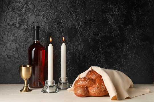 Traditional challah bread with wine and glowing candles on dark background. Shabbat Shalom