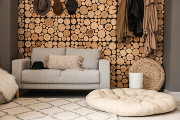 Comfortable sofa, pouf and hangers on wooden wall in room interior