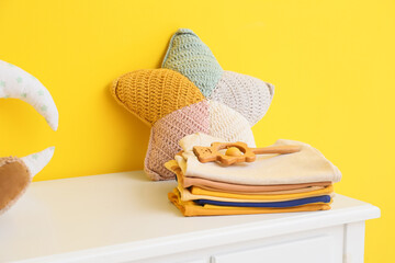 Stack of baby clothes with toys on table near yellow wall