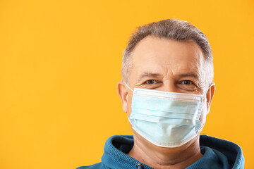 Senior man in medical mask on yellow background, closeup