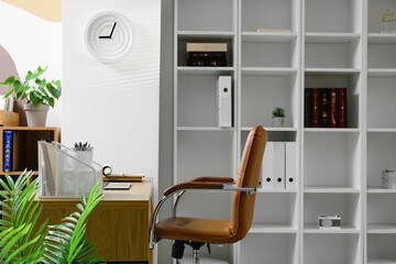 Comfortable workplace and stylish clock on light wall in office interior